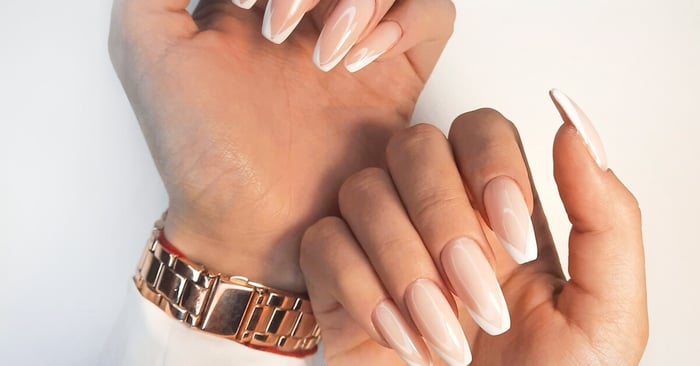 A close-up of gentle natural gel polish on long square nails with a French design. The lady is wearing a gold watch.
