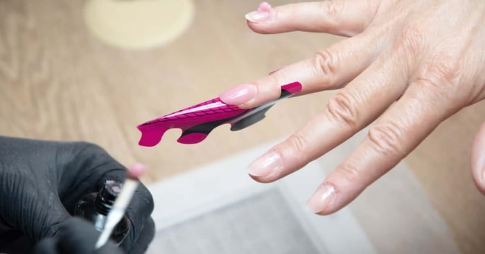 A nail technician is applying long acrylic nails to their client. They're using a gel acrylic builder sticker.