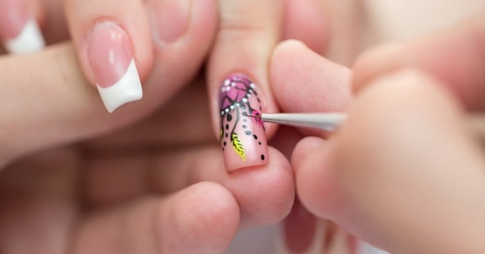 A nail technician is designing one of their clients' nails with black, white, pink, and yellow swirls, dots, and fine lines.