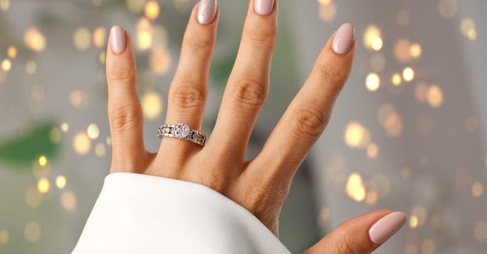 A close-up of a woman's left hand. She's wearing a diamond ring, and her nails are decorated with the soapy nail trend.