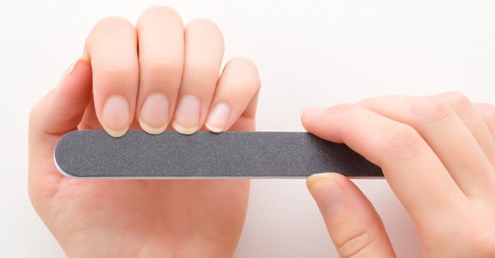At close range from a person's point of view, a woman shapes her nails using a black nail file above a clean, white table.