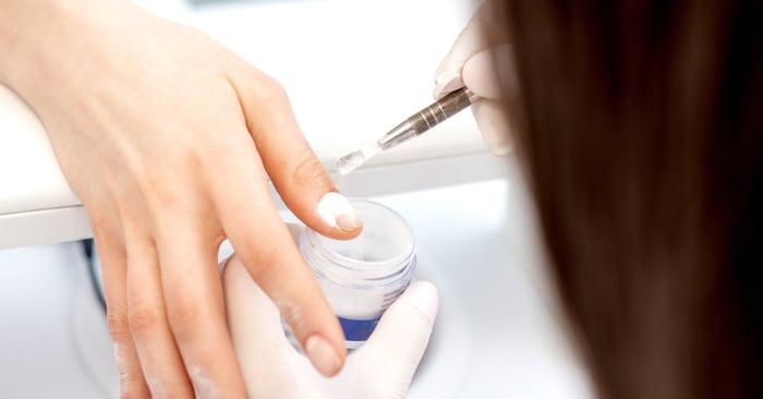 Technician applies acrylic powder to a woman's nails during a close-up beauty salon manicure session.