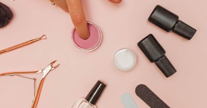 A woman dipping her fingernail in the colorful acrylic powder for a manicure. She also has other nail tools on display.