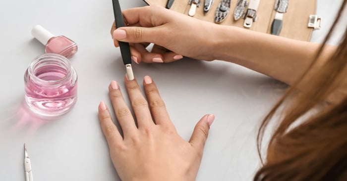 A close-up of someone doing their own manicure at home. They have a pink nail tool set out on the table.