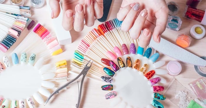 A person showing off their manicure with one decorated nail. The table is full of decorated faux nails and nail tools.