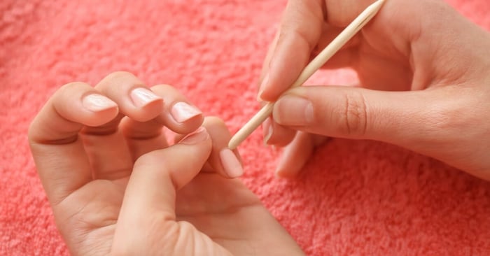 A close-up of a person working on their cuticles and removing light-colored nail polish over a pink-colored towel.