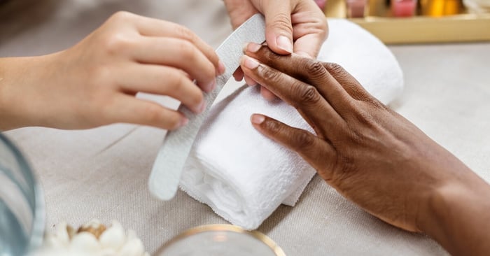 A professional nail technician using a board to file the ends of a customer's nails and achieve a smoother nail shape.