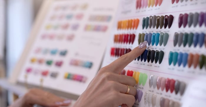 A person pointing out a specific display nail from two large boards of display nails, each with a different polish on it.