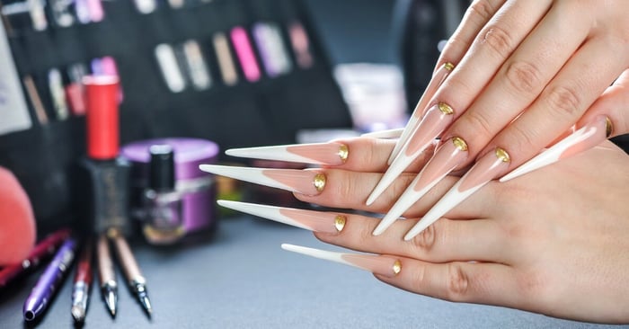 A nail client showing off their long stiletto-style nails with extended white French tips and gold cuticles.