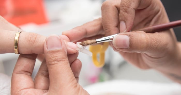 A close-up of a manicurist applying acrylic to the nail and nail form with a pin brush at a professional salon.