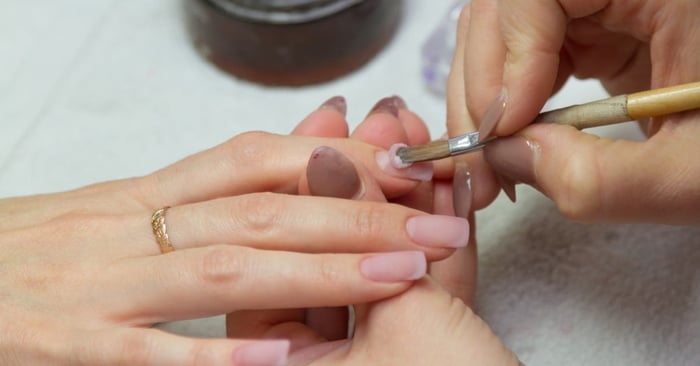 A close-up of a manicurist creating extension nails with acrylic pink powder in a professional nail salon.