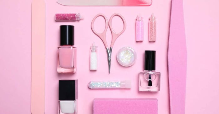 Various nail-care essentials, including scissors, polish, topcoat, glitter, and files, neatly organized on a pink background.