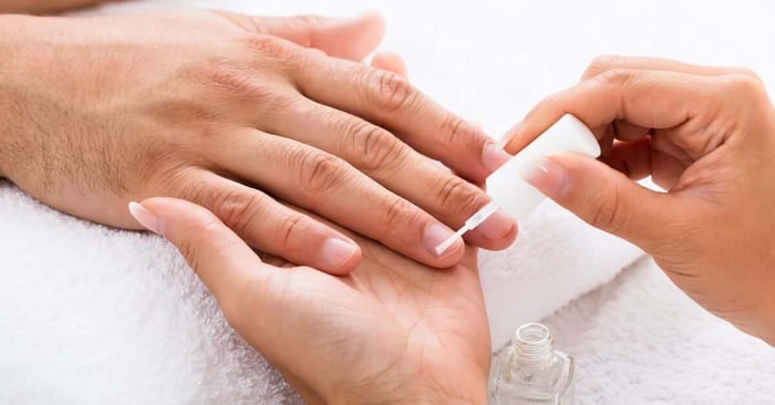 A close-up of a manicurist applying moisturizing fingernail oil on their client's nails. The towel is white.