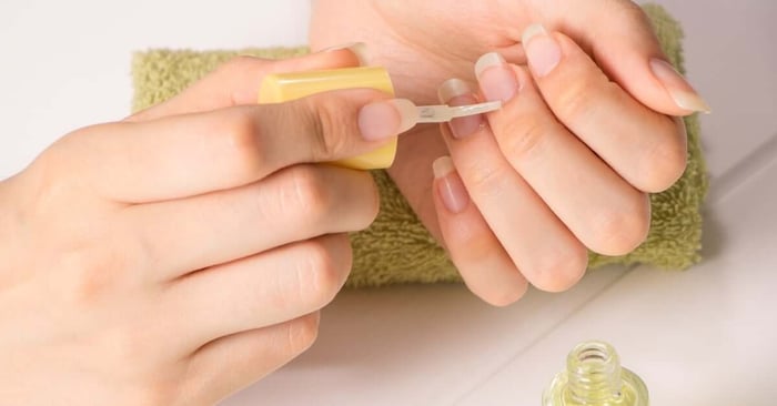 A close-up of a woman putting nail oil on her natural nail. Her nails don't have any polish on them.