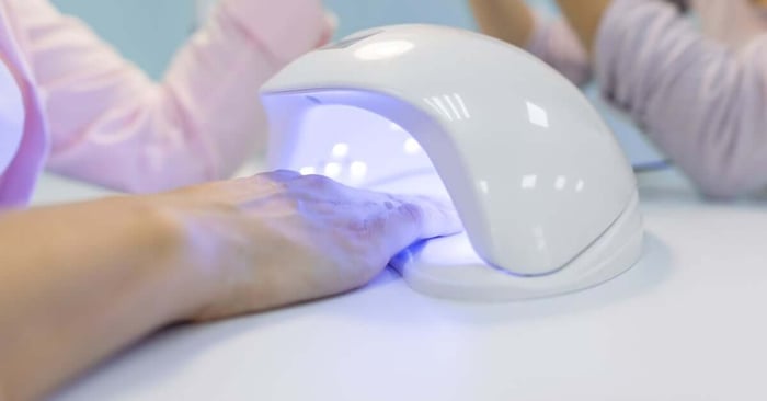 A person puts their right hand under an ultraviolet blue light lamp on a table to cure their manicure.