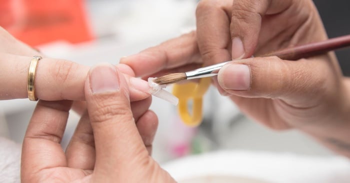 A manicurist holds their client's finger and sculpts acrylic onto their nail with a pinch brush.