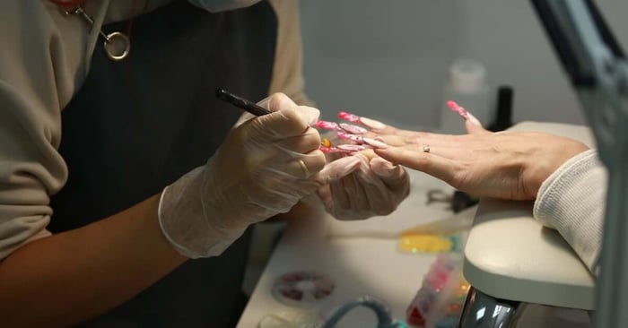 A technician applies long, colorful nail extensions on a client’s hand, sculpting length for an elegant finish.
