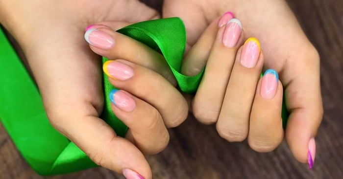 Two hands holding green fabric display pink manicured nails with colorful accent tips in yellow, blue, and purple.