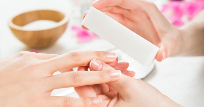 A manicurist files a client's nails with a white buffer during professional nail care treatment at a beauty salon.
