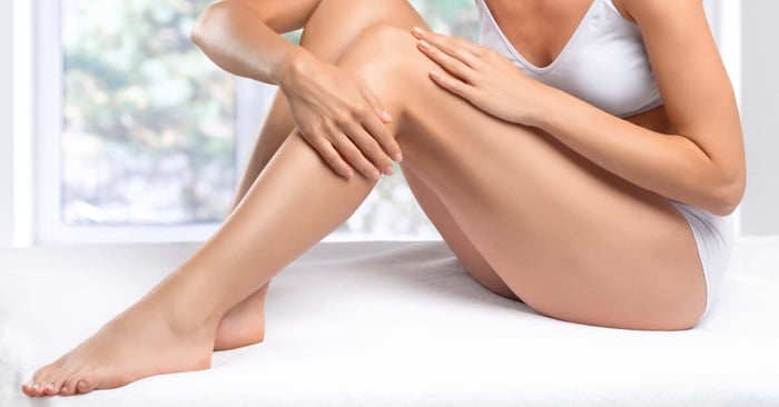 A woman in white underwear examines the smooth skin on her legs after a hair-removal treatment at a spa salon.