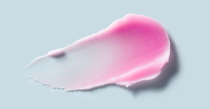 A pink cream wax smear on a light blue background, showing a smooth texture ideal for hair removal or skincare products.