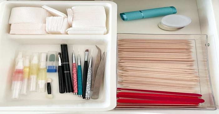 Organized nail supplies in a drawer with brushes, tools, wooden sticks, cotton pads, and nail files for professional manicures.