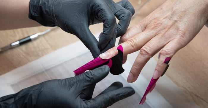 A nail technician applying a form to the end of a client's nail to more easily achieve a lengthened result with builder.