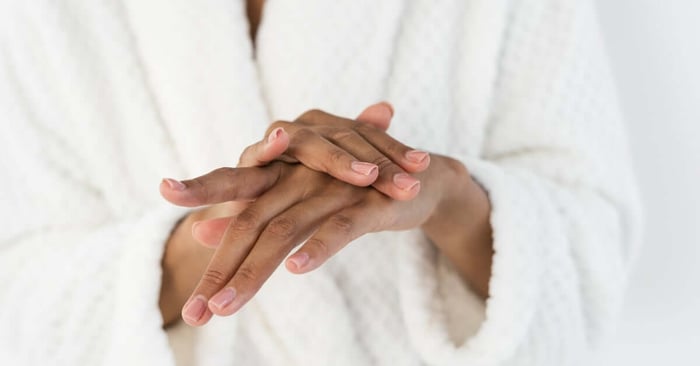 A person in a fluffy white robe rubbing one hand over the back of the other in a massaging motion for their skin.