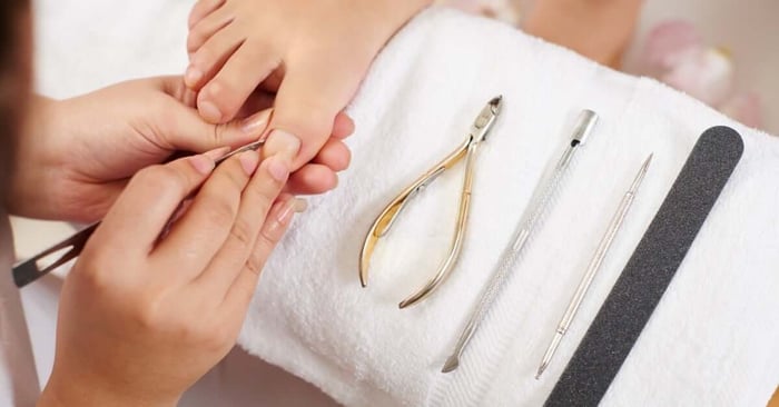 A professional nail technician using a tool to clean the sides of the nail bed on a client's big toe. Other tools sit on a towel.