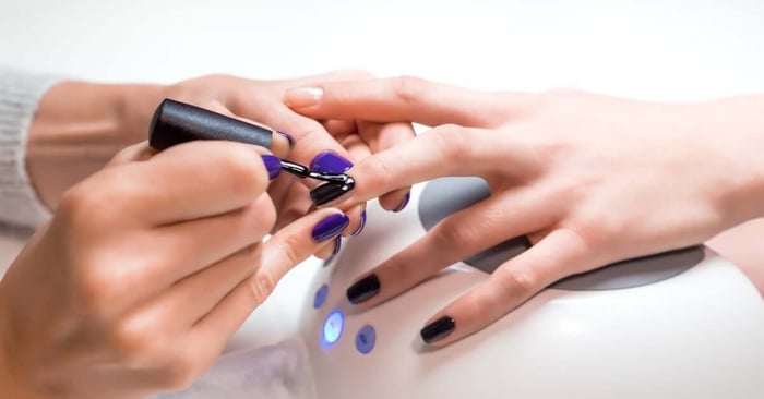 A nail technician applying a black gel nail polish onto a client's nails while their hand rests on a UV curing device.