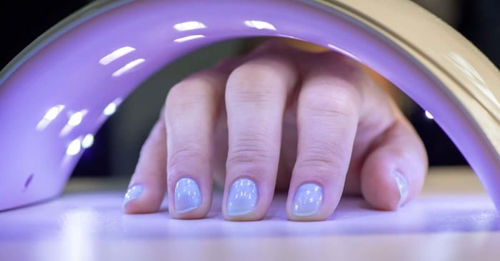 A client positioning their fingers beneath the lights inside a UV curing device to cure their pale nail polish.