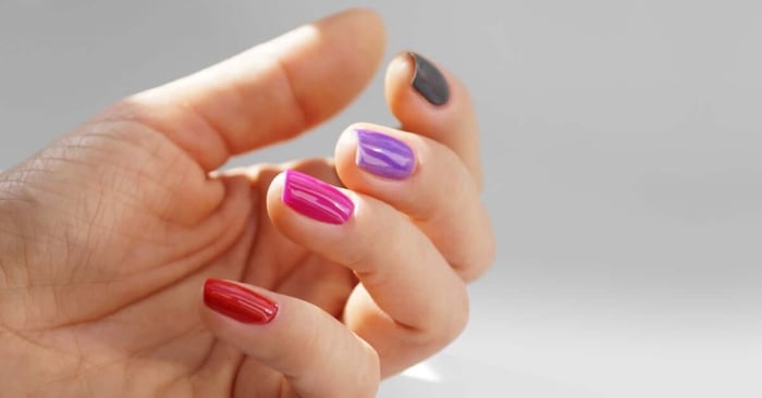 A person displaying their nails. Each nail has a different coat of gel polish, with colors from green to red.
