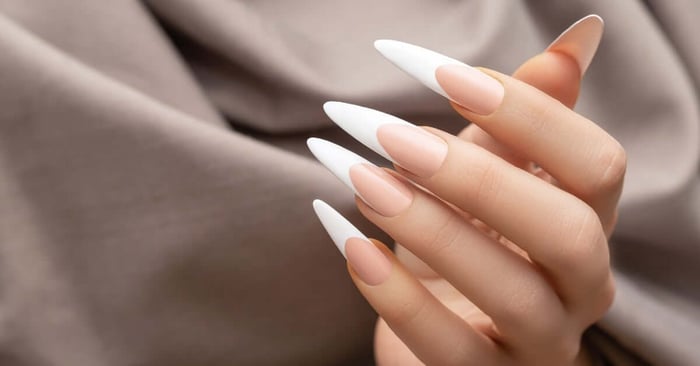 A close-up on a person's hands, emphasizing their long French tip nails, each in an extended almond shape.