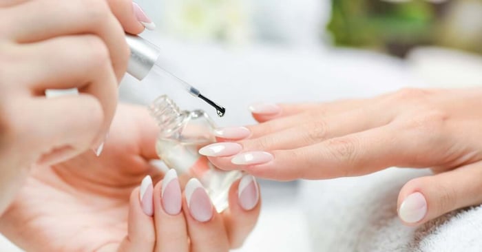 A professional manicurist with French tip nails applying a sealant over the gradient nails on a client's hand.