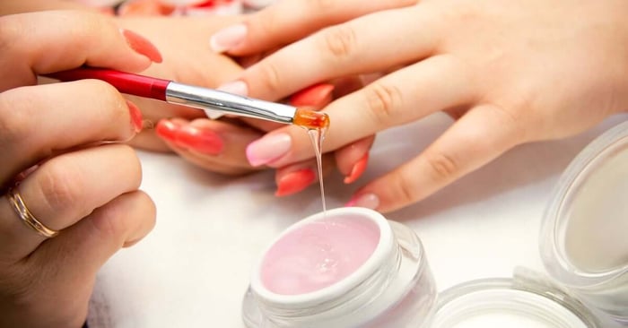 A manicure professional lifting a brush out of a pot of liquidy gel with an excessive amount dripping from the brush.