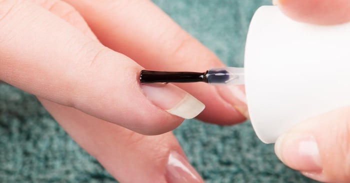 A close-up of a customer getting their natural long nail painted. The nail tech is applying clear nail polish.