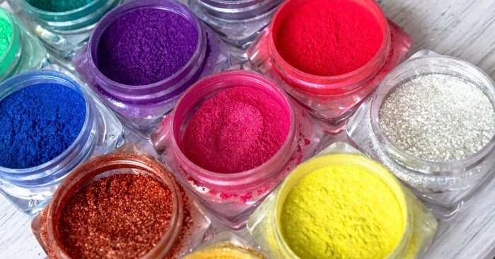 Small clear jars hold rainbow-colored glitter nail powders that are neatly arranged for use.