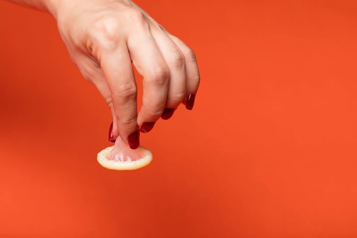 a hand holding the tip of a condom against an orange background