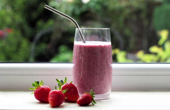 a pink smoothie next to strawberries on a window shelf