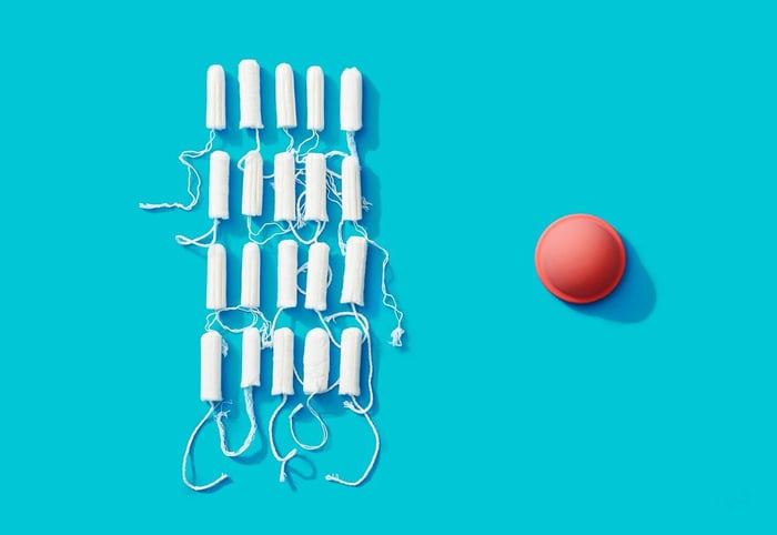 a pink menstrual disc to the right of multiple tampons against a blue background