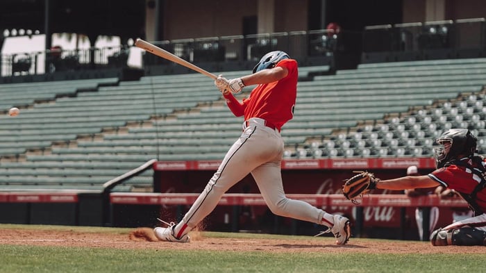 Baseball player using thumb guard swings at pitch during game, showcasing batting precision and protective gear