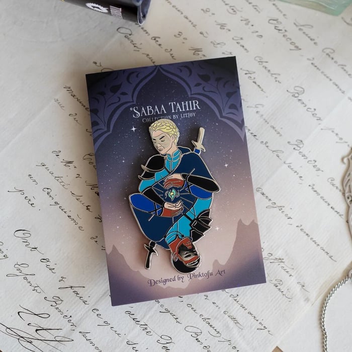 Helene and Avitas Enamel Pin has the two characters in masks appearing as a mirror of each other