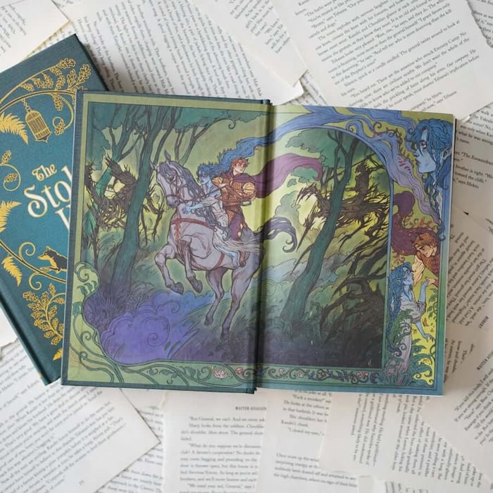 This image shows an open book with a detailed illustration on the page. The illustration depicts a scene with a person riding a horse through a forest, accompanied by another individual. The artwork is rich with colors and intricate designs, including trees and other elements of the forest. The book is placed on top of several other books and papers, suggesting a setting related to reading or study. The text around the illustration appears to be part of a story, with phrases and sentences visible on the surrounding pages.