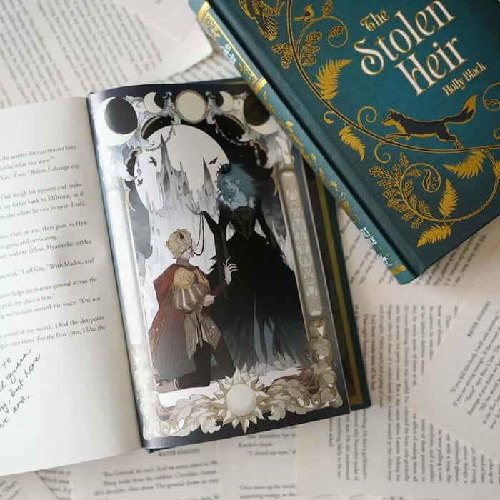 This image shows an open book displaying a page with text and an illustration. The illustration depicts a scene with two characters: one is a young boy dressed in red and gold, and the other is a woman with long green hair wearing a dark dress. The text on the page is written in a cursive font and includes dialogue and narrative. The book is placed on top of other books and papers, with one book prominently featuring the title "The Stolen Heir" by Holly Black on its cover. The cover has a green background with gold and white decorative elements.