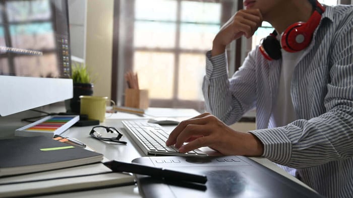 Editor at a desk with headphones reviewing work, representing project tracking and reporting in Asana
