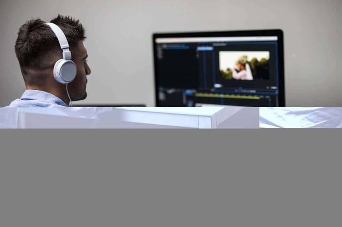 Editor working at a monitor with headphones, representing video project tracking in Trello