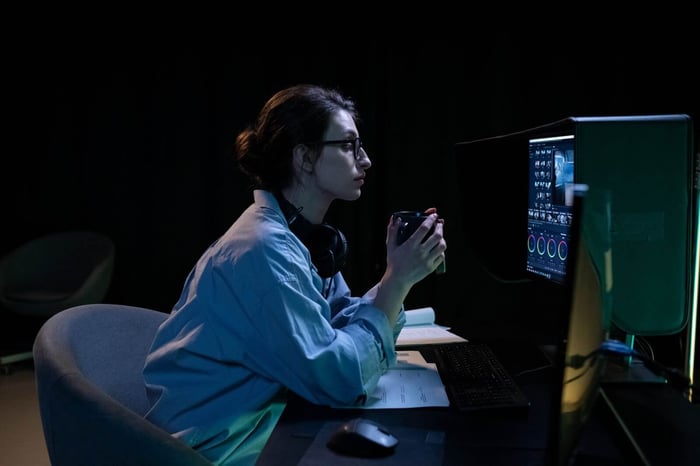 Editor working at a video editing workstation in a dim room, representing the frame by frame review involved in school surveillance video redaction