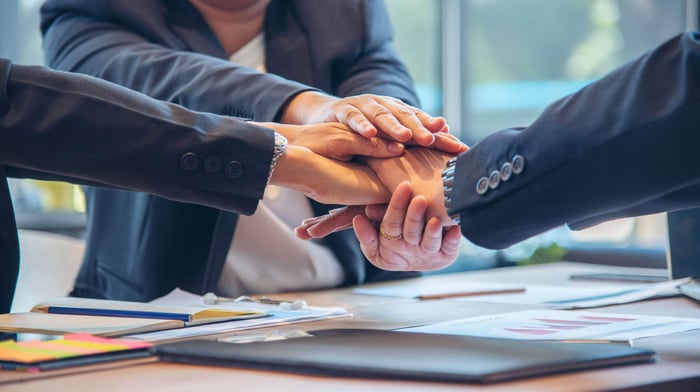 Hands stacked together over a desk, representing partnership between agencies and the public they serve