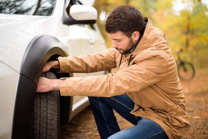 Homme vérifiant la condition de son pneu à l'extérieur pendant la saison d'automne