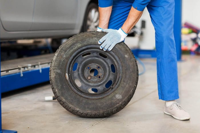 car service, repair, maintenance and people concept - auto mechanic man with wheel tire at workshop